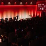 Dr Zack Ally explaining facial proportions during his presentation, with a projected anatomical diagram and an engaged audience.